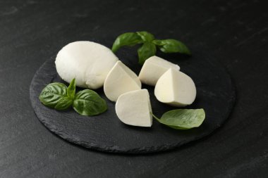 Lezzetli mozzarella peyniri ve fesleğen parçaları koyu dokulu masada, yakın plan.