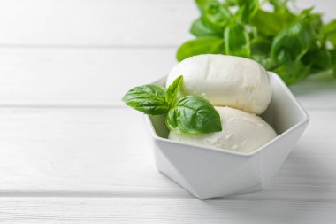 Lezzetli mozzarella peyniri ve fesleğen parçaları beyaz ahşap masada, yakın plan. Metin için boşluk