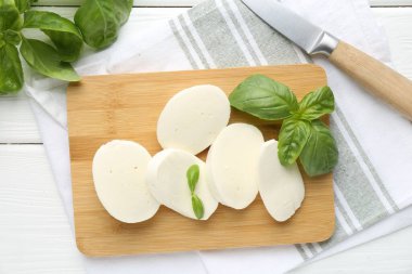 Lezzetli mozzarella peyniri parçaları, fesleğen yaprakları ve bıçak beyaz ahşap masa, düz yatıyordu.