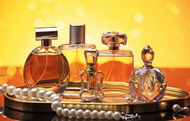 Ayna yüzeyinde turuncu arka planda birçok farklı parfüm şişesi ve aksesuar var.