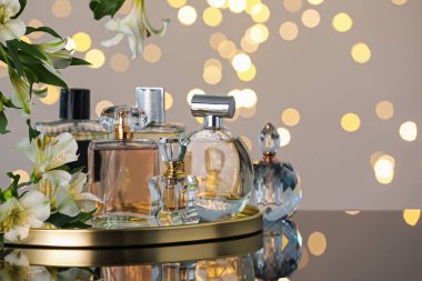 Ayna yüzeyindeki birçok farklı parfüm şişeleri ve çiçekler açık gri arka planda bulanık ışıklara karşı, yakın plan. Metin için boşluk