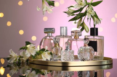 Ayna yüzeyinde birçok farklı parfüm şişesi ve çiçek var. Pembe arka plan, bulanık ışıklar, yakın plan.