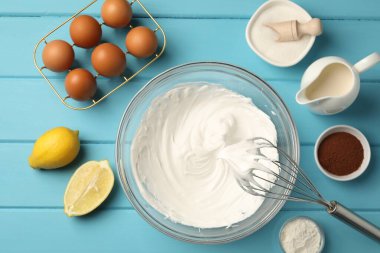 Açık mavi ahşap masada çırpılmış krema, yumurta ve diğer ürünlerle çırpın.