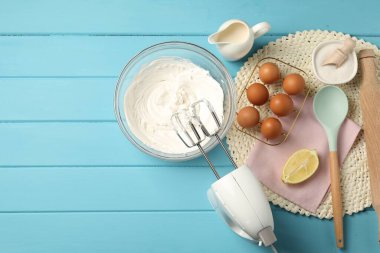 Açık mavi ahşap masa üzerinde çırpılmış krema, yumurta ve diğer ürünlerle el çırpma makinesi. Metin için boşluk