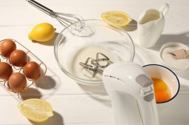 El çırpıcı, kasede yumurta beyazı, beyaz ahşap masada yumurta ve diğer ürünler.