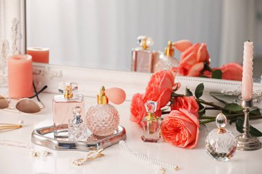 Farklı parfüm şişeleri, aksesuarlar ve çiçekler kapalı salonda.