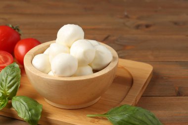 Lezzetli mozarella topları, domatesler ve fesleğenler ahşap masada, yakın plan.