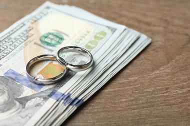 Gümüş alyanslar ve dolar banknotları ahşap masada, yakın plan. Metin için boşluk