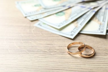 Altın alyanslar ve dolar banknotları ahşap masada, yakın plan. Metin için boşluk