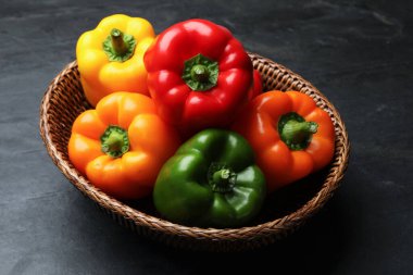 Hasır sepetin içinde taze renkli dolma biberler siyah desenli masada, yakın plan.