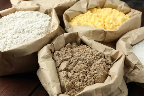 Tahta masadaki kağıt torbalarda farklı türde un, yakın plan.