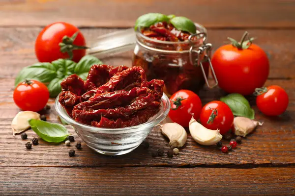 Lezzetli güneş, cam bulaşık takımında kurutulmuş domatesler, ahşap masada taze sebzeler ve baharatlar, yakın plan.