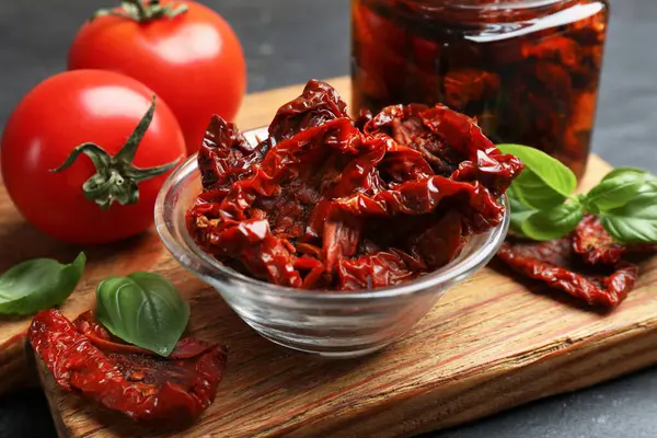 Lezzetli güneşte kurutulmuş domatesler ve taze sebzeler siyah masada, yakın plan.