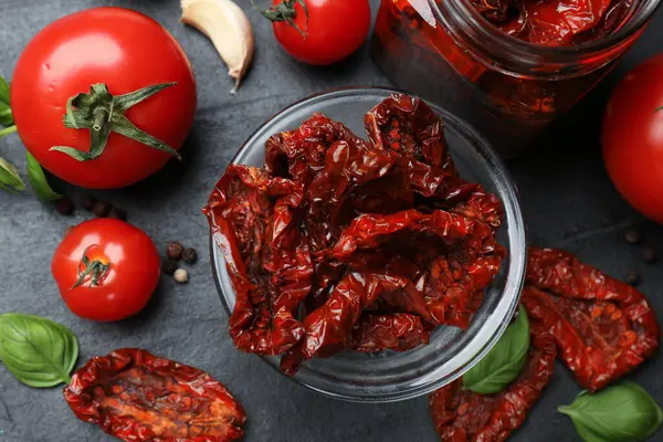 Lezzetli, kurutulmuş domatesler, taze sebzeler ve siyah masada biberler, düz uzanmış.