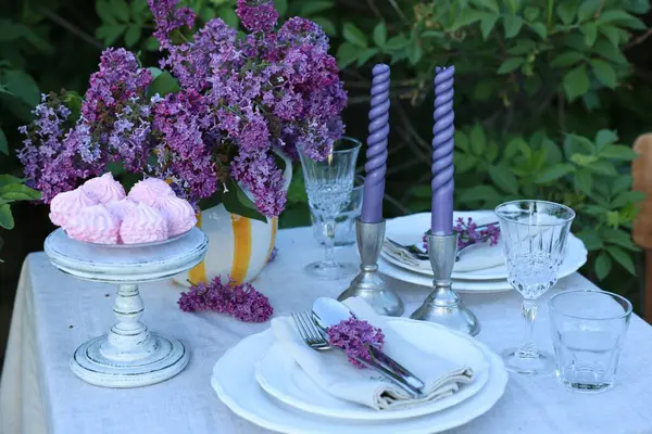 Güzel leylak çiçekleri, zephyrler, tabaklar, çatal bıçaklar, bardaklar ve mumlar bahçede.
