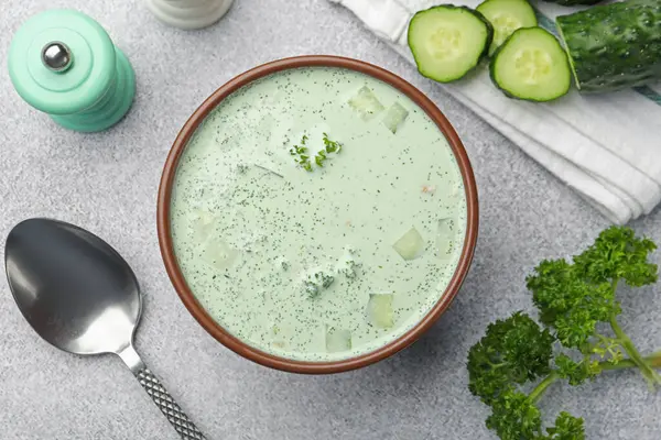 Lezzetli salatalık çorbası ve açık gri masada bulunan malzemeler.