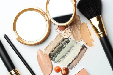 Farklı kozmetik ürünleri, makyaj fırçaları ve beyaz arka planda ayna, düz yatış