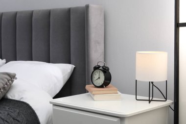 İçinde lamba, çalar saat ve yatağın yanında kitaplar olan komodin.