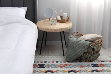 Yan masada ayna, çalar saat ve yatağın yanında dekor var.