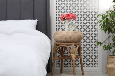 Çalar saati olan yan masa ve yatağın yanında çiçekler.