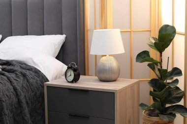 İçeride yatağın yanında çalar saat ve lamba olan komodinin yanında.