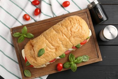 Mozarella peynirli, domatesli, fesleğenli ve baharatlı lezzetli sandviç siyah ahşap masada, düz yatıyordu.