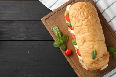 Mozarella peynirli, domatesli, fesleğenli, siyah ahşap masa manzaralı lezzetli bir sandviç. Metin için boşluk