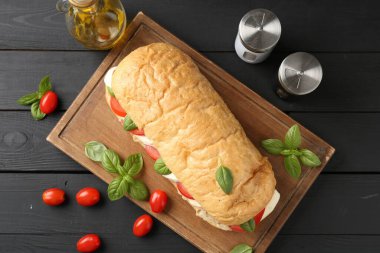 Mozarella peynirli, domatesli, fesleğenli ve baharatlı lezzetli sandviç siyah ahşap masada, düz yatıyordu.