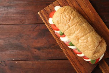 Mozarella peynirli, domatesli ve ahşap masadaki fesleğenli lezzetli sandviç. Metin için boşluk