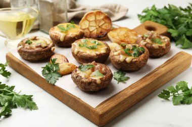 Eritilmiş peynirli, sarımsaklı ve maydanozlu lezzetli mantarlar beyaz masada, yakın plan.