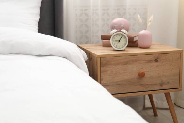 Yatağın yanında alarm saati ve dekorasyonu olan komodinin yanında.