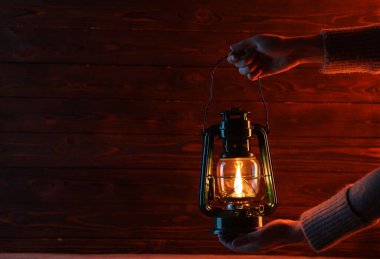 Ahşap duvarın yanında eski model gaz lambası tutan kadın, yakın plan. Metin için boşluk