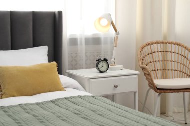 Yatağın yanında lamba ve çalar saat olan komodinin yanında.