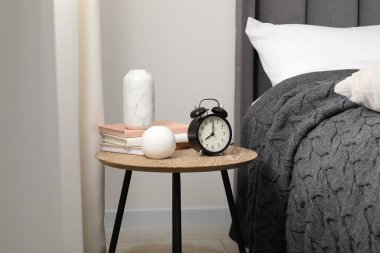 Yatağın yanında alarm saati ve dekorasyonu olan komodinin yanında.