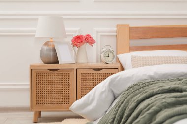 İçinde lamba, çalar saat ve yatağın yanında çiçekler olan komodin.