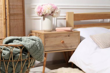 Yatağın yanında kitaplar ve çiçekler olan komodin.