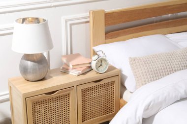 İçinde lamba, çalar saat ve yatağın yanında kitaplar olan komodin.