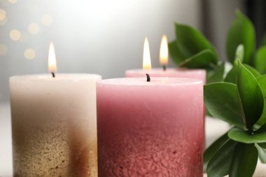 Masada yanan mumlar ve yeşil yapraklar bulanık ışıklara karşı, yakın çekim