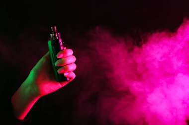 Siyah arka planda neon ışıklarda elektronik sigara içen bir kadın, yakın plan. Metin için boşluk