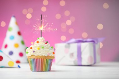 Pembe arka planda bulanık ışıklarla kek ve parti dekorunda yanan maytap. Metin için boşluk