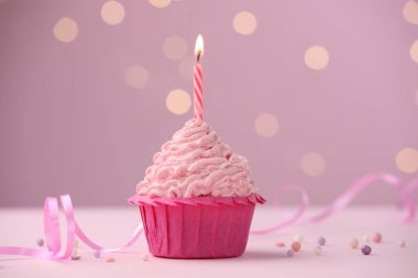 Kekin içinde yanan mum. Masanın üzerinde. Pembe arka plan ve bulanık ışıklar.