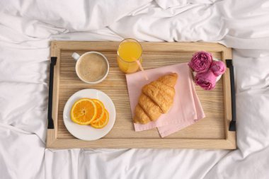 Nefis bir kahvaltı tepsisi ve yatağın üstünde çiçekler, üst manzara.