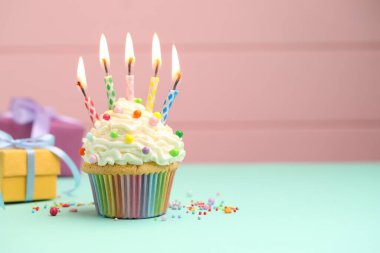 Kekin içinde mum yakmak, turkuaz masa üzerinde hediye kutuları pembe arka planda, metin için boşluk