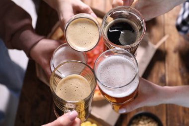 Arkadaşlar masada bira bardaklarını tokuşturur, yakın plan