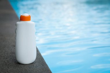 Yüzme havuzunun yakınındaki taş yüzeyde bir şişe güneş koruması ürünü, metin için yer