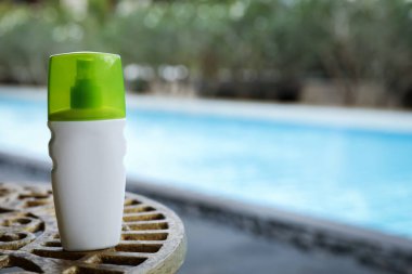 Yüzme havuzunun yanındaki masada bir şişe güneş koruması ürünü, metin için yer var.