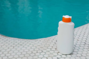 Yüzme havuzu yakınında bir şişe güneş koruması ürünü, yazı için yer