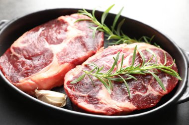 Gri masadaki pişirme kabında çiğ et ve baharat parçaları, yakın plan.