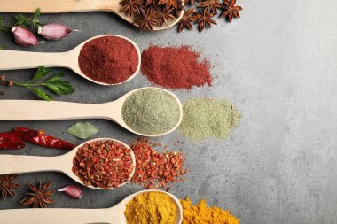 Gri masadaki kaşıklardaki farklı baharatlar düzdü.