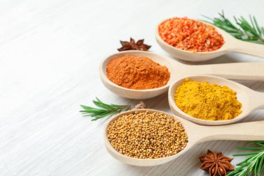 Beyaz ahşap masadaki kaşıklardaki farklı aromatik baharatlar, yakın plan. Metin için boşluk